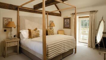 A four-poster bed with a wooden frame, two bedside tables with lamps, a large mirror, and a window with curtains.