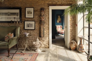 A room with a stone wall, a green armchair, a small table with a bowl, and a doorway leading to another room.
