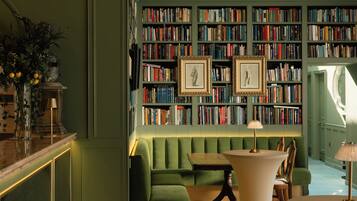 Una biblioteca con estanterías, un sofá verde, una mesa y dos cuadros enmarcados.
