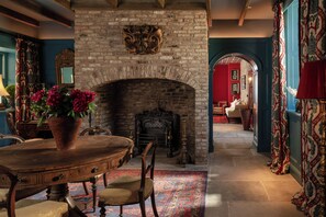 A room with a brick fireplace, a wooden table with chairs, and a patterned rug.
