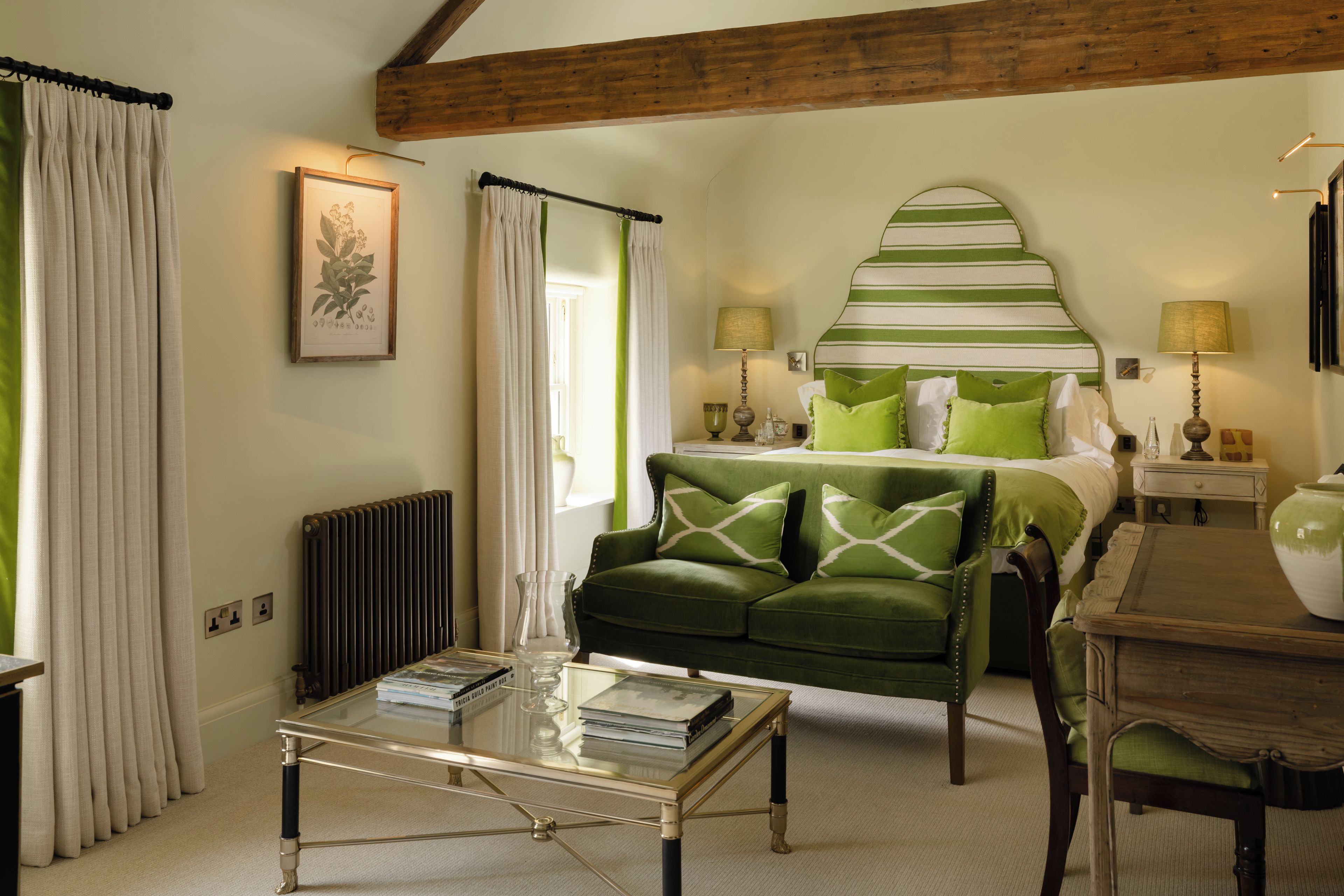 Una habitación con una cama, un sofá verde, una mesa de centro de vidrio y un radiador.