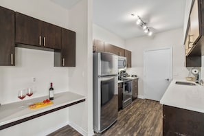 A compact kitchen with dark wooden cabinets, a stainless steel refrigerator, and a microwave. - Bright 2-bedroom apartment with AC in beautiful Dallas (Dallas)