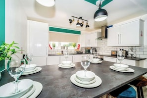 A modern kitchen with white cabinets, a dark countertop, and a dining area set for six with plates and glasses.