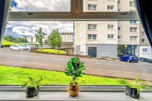 A window view of a parking lot with several cars, a grassy area, and a building with multiple windows and balconies.