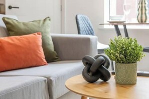 Una sala de estar con un sofá gris, una mesa de centro redonda de madera y una planta en maceta.