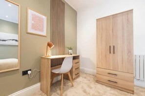 A bedroom with a bed, a desk with a chair, a wardrobe, and a wall-mounted shelf. - Stylish Leeds Retreat | 1BR with Parking (Leeds)