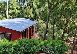 A red building with a metal roof, surrounded by dense greenery and trees. - Reveridge Flora Cottage 3BH Matheran (Matheran)