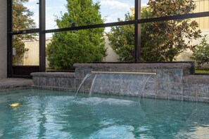 A swimming pool with a waterfall feature, surrounded by a stone wall and greenery. - 4BR Le Reve Townhome Pool & Themed Rooms (Kissimmee)