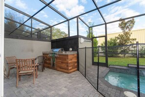 A covered patio with a barbecue grill, seating area, and a view of a swimming pool. - 4BR Le Reve Townhome Pool & Themed Rooms (Kissimmee)