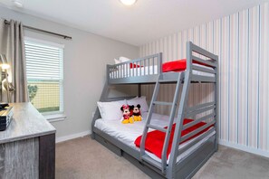 Ein Etagenbett mit Mickey Mouse Plüschtieren, ein Schreibtisch mit Lampe und ein Fenster mit Jalousien.