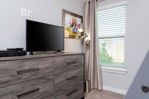 Ein Zimmer mit einem Flachbildfernseher auf einer Holzkommode, einem gerahmten Bild an der Wand und einem Fenster mit Jalousien.