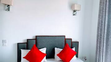 A hotel room with a bed, two red pillows, a grey headboard, and a grey curtain.