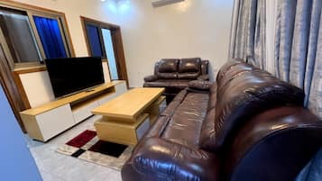 Una sala de estar con un sofá de cuero, una mesa de centro de madera y un televisor de pantalla plana.
