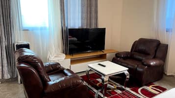 A living room with a flat-screen TV, two leather sofas, a coffee table, and a red patterned rug.