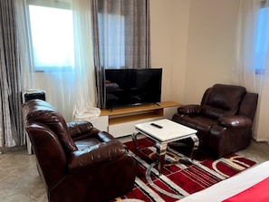 Una sala de estar con televisor de pantalla plana, dos sofás de cuero, una mesa de centro y un tapete estampado rojo.