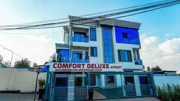 Un edificio de varios pisos con un letrero que indica 'COMFORT DELUXE APARTMENT', señalando que ofrece alojamiento, bebidas y servicio de comidas.