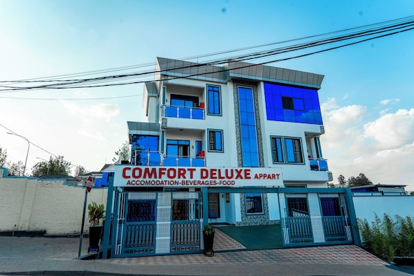 Un edificio de varios pisos con un letrero que indica 'COMFORT DELUXE APARTMENT', señalando que ofrece alojamiento, bebidas y servicio de comidas.