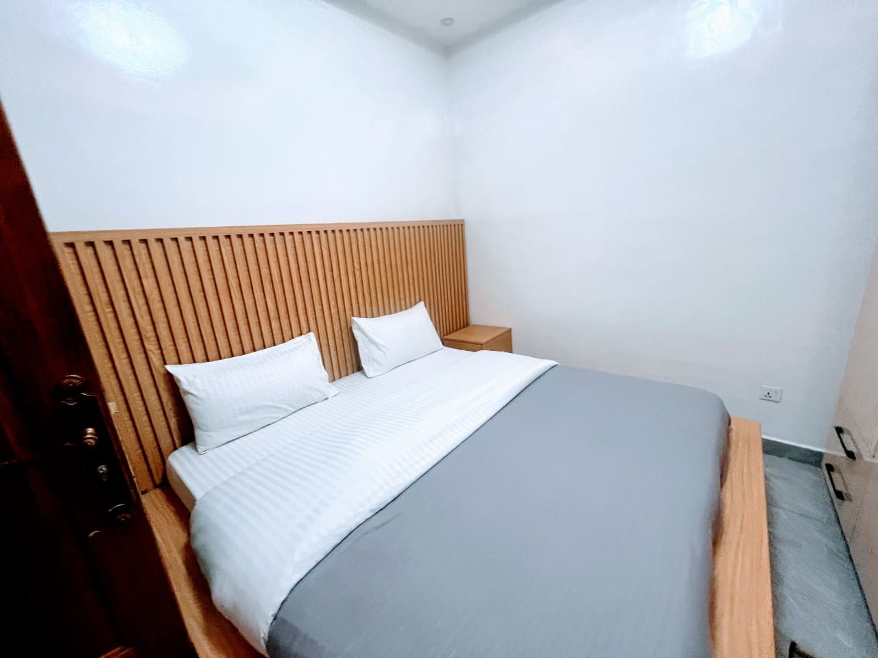 Un dormitorio con cama, cabecera de madera, mesitas de noche y una mesilla.