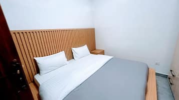 Un dormitorio con cama, cabecera de madera, mesitas de noche y una mesilla.