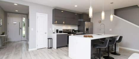 A modern kitchen with a central island, bar stools, and a staircase leading to another level.