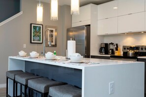 A modern kitchen with a central island, bar stools, stainless steel appliances, and pendant lighting. - 4BR Near Disney Private Pool, Themed Rooms (Kissimmee)