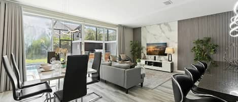 A modern living room with a dining area, large windows, and a flat-screen TV.