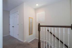 A hallway with a carpeted floor, a white door, a mirror with a gold frame, and a window with blinds. - 4BR Townhome Near Disney Pool & Mickey Room (Kissimmee)