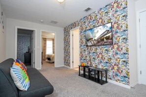 A living room with a large TV, a couch with colorful pillows, and a wall covered in comic book-style wallpaper. - 4BR Townhome Near Disney Pool & Mickey Room (Kissimmee)