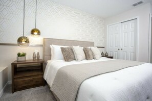 A bedroom with a bed, a nightstand, a wall-mounted lamp, and a door. - 5BR Solara Home Private Pool & Themed Rooms (Kissimmee)