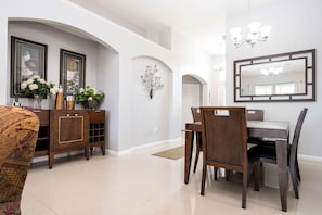 A dining area with a wooden table and chairs, a cabinet with decorative items, and a large mirror on the wall. - 4BR Windsor Palms Pool, spa & Mickey Room (Kissimmee)