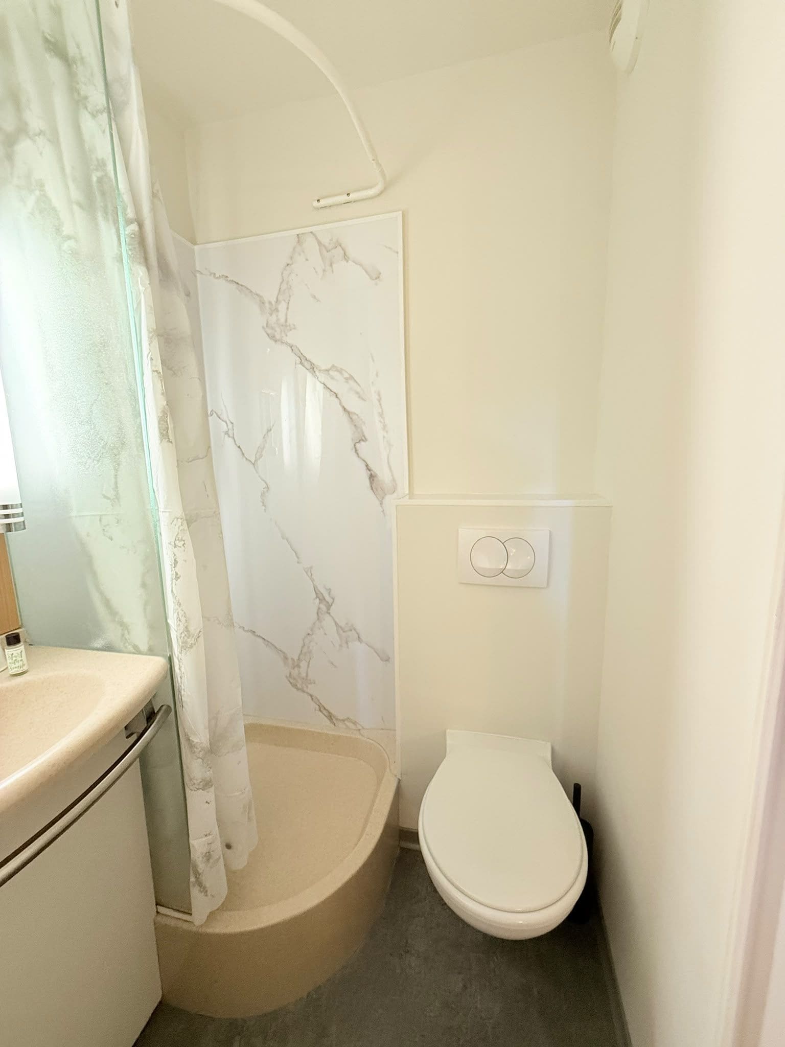 Un baño con inodoro, ducha con pared de mármol y lavamanos.