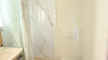 Un baño con inodoro, ducha con pared de mármol y lavamanos.