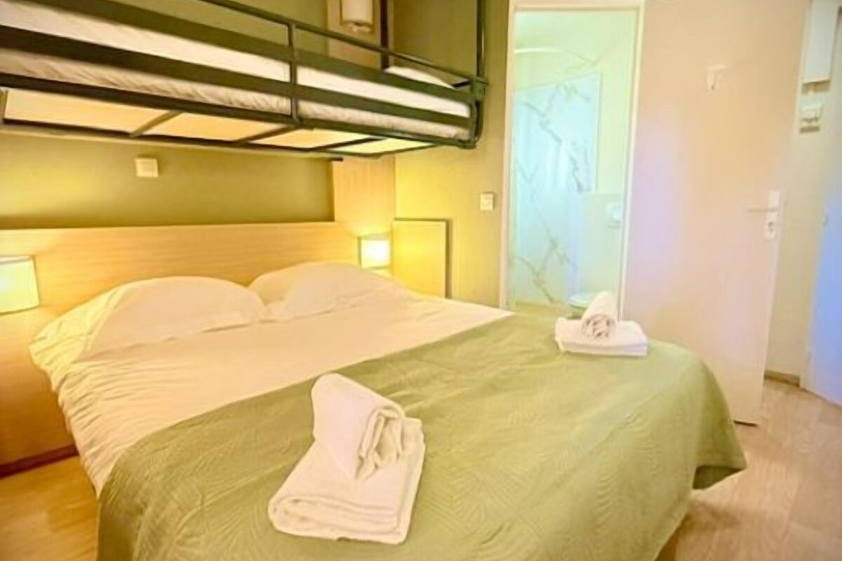Una habitación de hotel con una litera, un edredón verde y una toalla doblada en la cama.