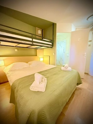 Una habitación de hotel con una litera, un edredón verde y una toalla doblada en la cama.