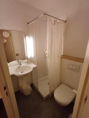 A bathroom with a shower, toilet, sink, and a mirror.