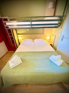 Una cama litera con dos almohadas y una colcha verde. Hay dos lámparas de noche y una toalla sobre la cama.