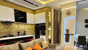Una sala de estar moderna con un sofá modular, una mesa de centro y electrodomésticos integrados en la cocina.