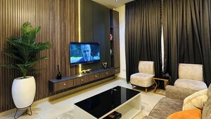 Uma sala de estar moderna com televisão de tela plana, uma mesa de centro, sofás e uma luminária decorativa no teto.