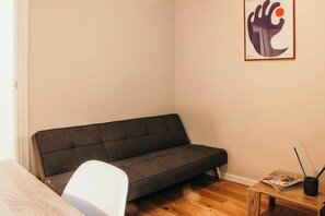 A small room with a grey sofa, a white chair, a wooden table with a magazine, and a framed artwork on the wall. - Urban Suite - Lakeside L&b (Milano)