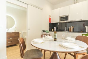 A modern kitchen with white cabinets, a built-in microwave, and a dining area with a round table set for four. - Cica Studio by Atlantic Holiday (Santa Cruz)