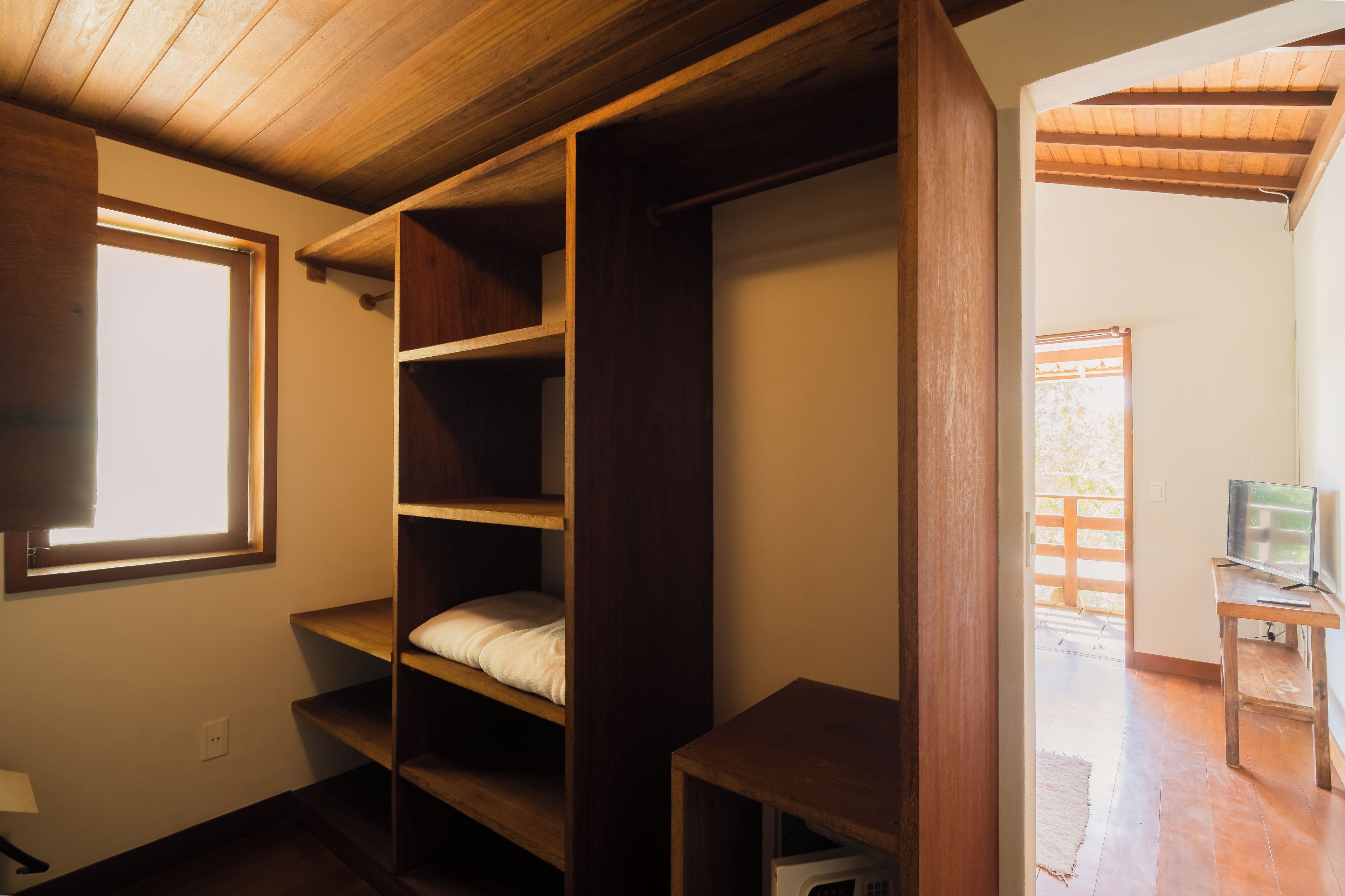 Quarto com estantes de madeira, uma janela e uma televisão sobre um suporte.