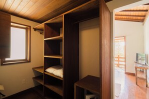 Quarto com estantes de madeira, uma janela e uma televisão sobre um suporte.