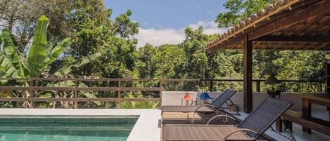 A poolside area with lounge chairs, a pergola, and a view of lush greenery.
