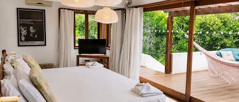 A bedroom with a large bed, a television on a stand, and a view of a lush garden through a sliding glass door.