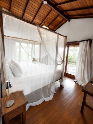 Un dormitorio con cama a dosel, suelo de madera y vistas al exterior con vegetación.