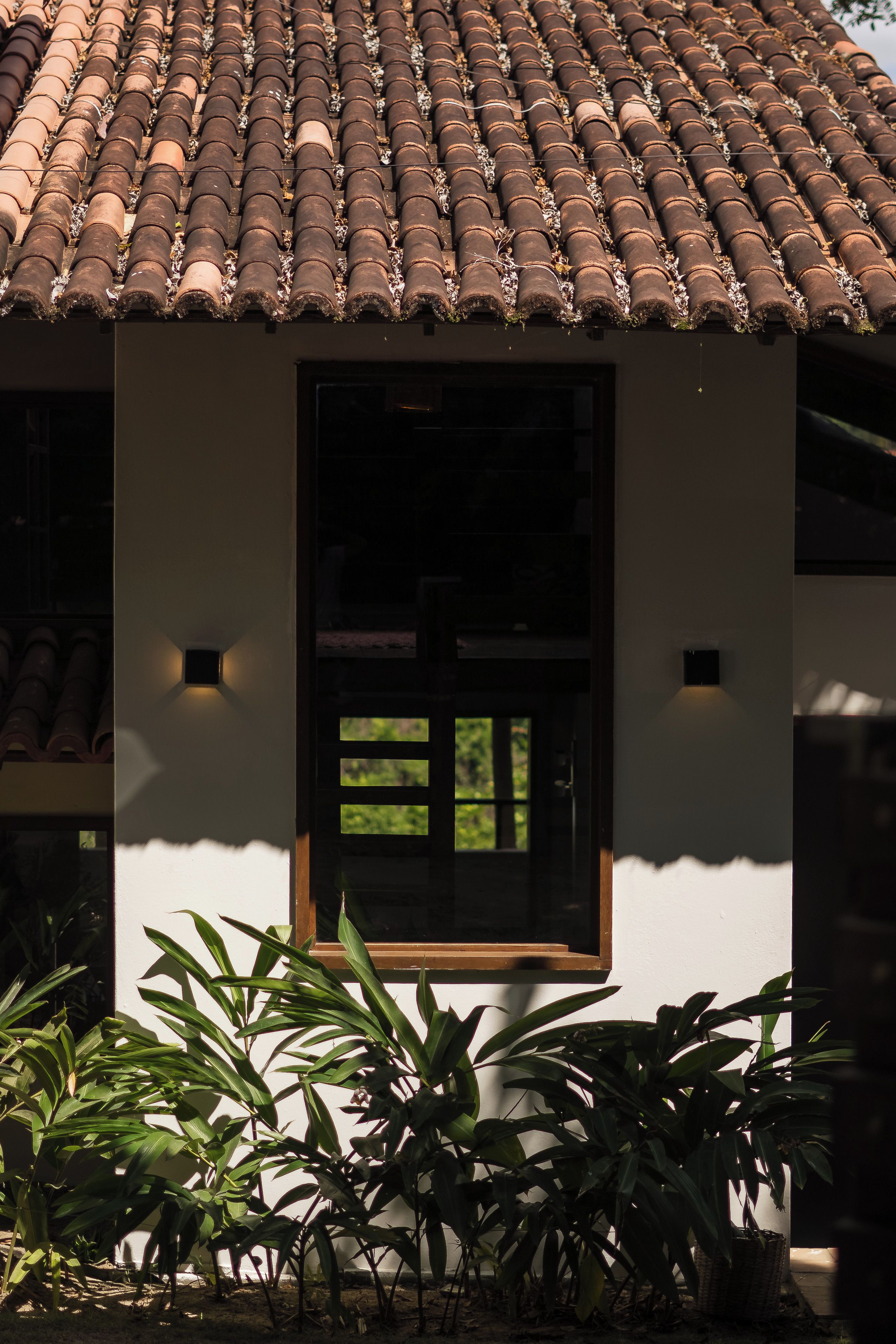 A building with a tiled roof, a window with a wooden frame, and a wall-mounted light fixture.