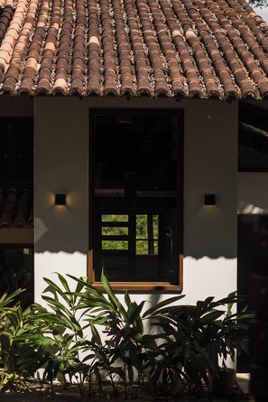 Um edifício com telhado ladrilhado, janela emoldurada por madeira e luminária fixada na parede.