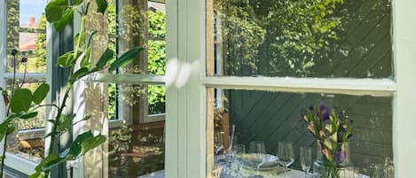 A room with large windows, a dining table set with glassware, and a hanging light fixture.