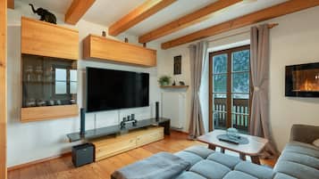 Ein modernes Wohnzimmer mit einem Flachbildfernseher, Holzschränken, einer Vitrine mit Weingläsern, einem Sofa und einem Fenster mit Vorhängen.