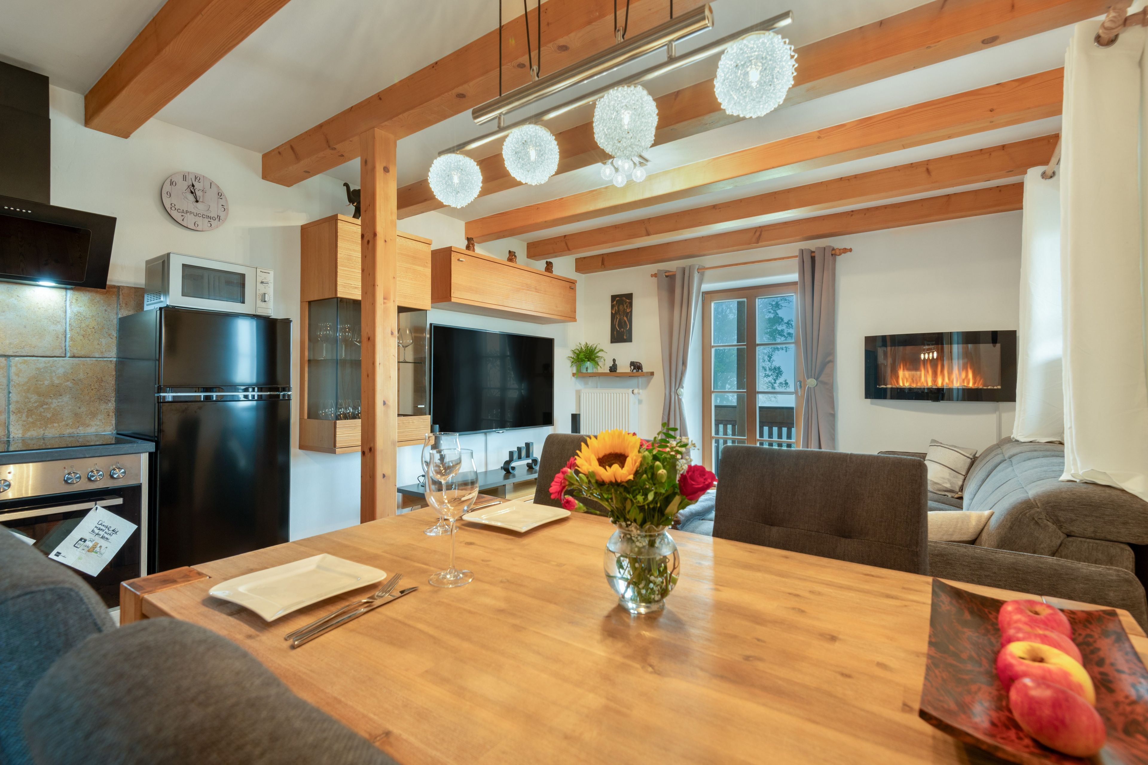 A modern kitchen with a built-in oven, microwave, and a wooden dining table with a vase of flowers.